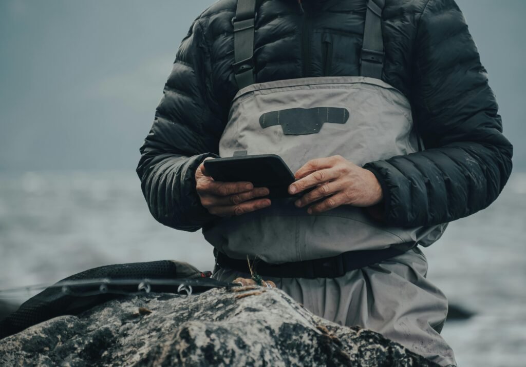 Homme en tenue de protection utilisant une tablette avec des gants dans un environnement extérieur froid et brumeux. Idéal pour les thèmes de la technologie et de l'aventure en plein air.