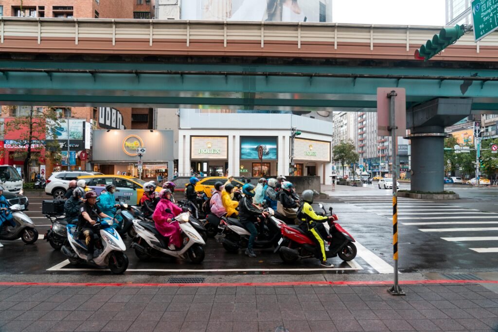 Group of people on scooters waiting at a city intersection under a bridge.